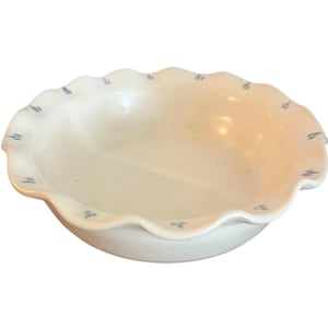 Peut inclure: Un bol en céramique blanc avec un bord festonné. Le bord est orné de petits motifs bleus en forme de feuilles. Le bol a une forme peu profonde et arrondie, adaptée au service ou à l'exposition.