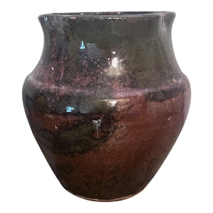 May include: A handcrafted ceramic vase with a unique, organic shape. The vase features a gradient of colors, transitioning from a dark, earthy green at the top to a rich, reddish-brown at the base. The surface has a textured, speckled appearance.