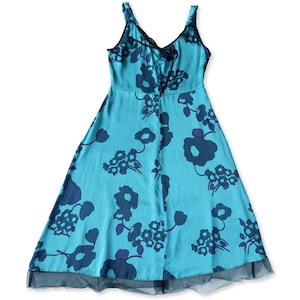 May include: A turquoise dress with a floral pattern in shades of blue. The dress has a V-neckline with black trim and a flared skirt. The hemline is finished with a black mesh detail. The dress is sleeveless and made of a lightweight fabric.