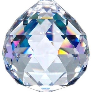 May include: A clear, faceted crystal ball with a complex geometric design. The crystal reflects light, displaying a spectrum of colors including blue, yellow, and pink. The ball is a decorative object.