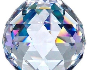 May include: A clear, faceted crystal ball with a complex geometric design. The crystal reflects light, displaying a spectrum of colors including blue, yellow, and pink. The ball is a decorative object.