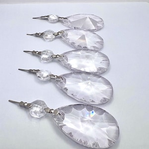 May include: Five clear crystal teardrop shaped chandelier prisms with silver metal connectors. Each prism has a faceted design and a silver metal connector.