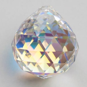 Op de afbeelding: Een heldere kristallen bol met een facetgeslepen ontwerp. De bol is iriserend en reflecteert licht in een regenboog van kleuren.