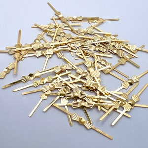 Könnte beinhalten: Eine Sammlung kleiner, goldfarbener dekorativer Metallspieße. Jeder Spieß hat ein Design in Form einer Fliege mit einem sechseckigen Mittelteil und radialen Linien. Die Spieße sind auf einer weißen Oberfläche verstreut und bilden eine ansprechende Anordnung.