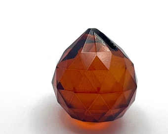 May include: A faceted amber glass ball ornament with a pointed top. The ornament is a deep orange color and has a shiny finish.