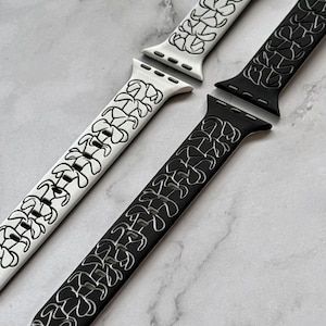 Puede incluir: Se muestran dos correas para Apple Watch, una blanca y otra negra. Ambas correas presentan un diseño floral estilizado y repetitivo en colores contrastantes. Las correas están hechas de un material flexible y están diseñadas para adaptarse a un Apple Watch estándar.