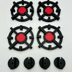 Peut inclure: Un ensemble de grilles de brûleur de cuisinière et de boutons de commande noirs et rouges. Les grilles sont circulaires avec un centre rouge et un design géométrique. Les boutons sont noirs avec un trait indicateur blanc.