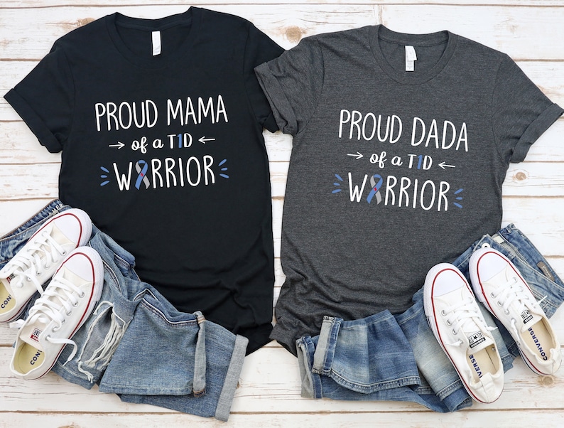 May include: Two t-shirts, one black and one gray, with the text "Proud Mama of a TID Warrior" and "Proud Dada of a TID Warrior" on them. Both shirts feature a blue and gray ribbon.