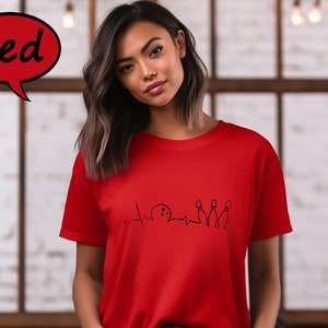 Puede incluir: Una camiseta roja con un gr&aacute;fico negro de una bola de bolos y bolos con una l&iacute;nea de latido del coraz&oacute;n.
