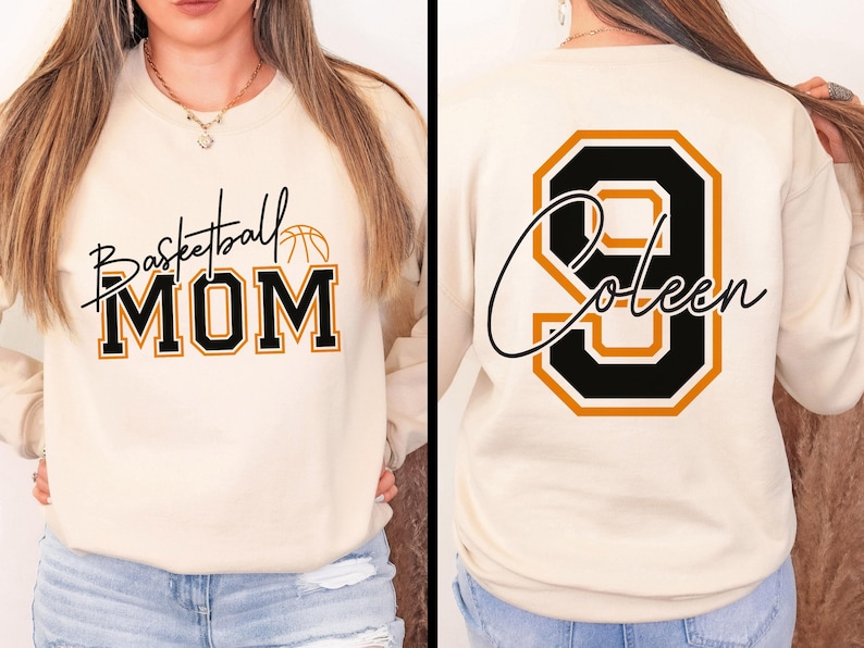 May include: Cream-colored sweatshirt with the text "Basketball MOM" in black and gold lettering, with a basketball graphic. The back of the sweatshirt features the number "9" and the name "Coleen" in a similar style.