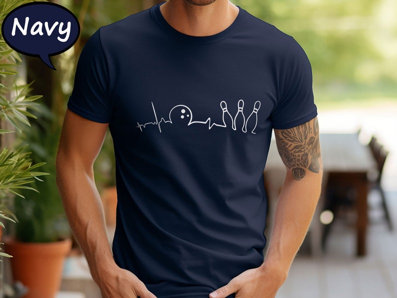 May include: A navy blue t-shirt with a white graphic of a heartbeat with a bowling ball and pins. The graphic reads 'Bowling is my therapy'.