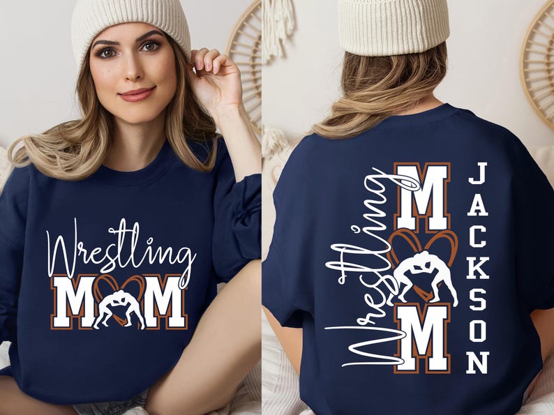 以下が含まれることがあります： ネイビーブルーのスウェットシャツ。白の筆記体とブロック体で「Wrestling MOM」の文字とレスリングのグラフィックが描かれています。シャツの背面には、白で「Wrestling MOM」と「Jackson」の文字が書かれています。