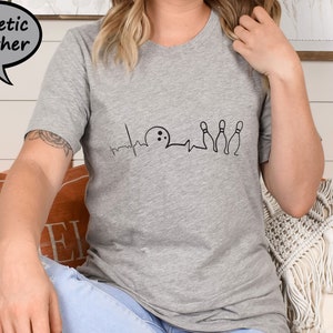 Puede incluir: Una camiseta gris jaspeada con un gr&aacute;fico negro de una bola de bolos y bolos con una l&iacute;nea de latido del coraz&oacute;n. El gr&aacute;fico dice "Bowling is my therapy".