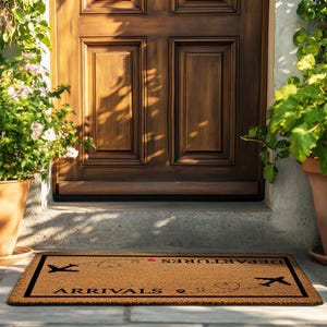 May include: A rectangular doormat with the words "ARRIVALS" and "DEPARTURES" in black text. The mat is brown with a black border and features airplane graphics. The mat is placed in front of a wooden door, with potted plants on either side.