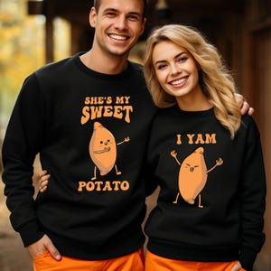 Puede incluir: Sudaderas negras con dise&ntilde;os a juego. Una dice "She's My Sweet Potato" con una batata de dibujos animados. La otra dice "I Yam" con una batata de dibujos animados. Una pareja sonriente lleva las sudaderas.