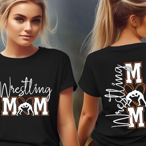 以下が含まれることがあります： 黒いTシャツ。白い筆記体とブロック体の文字で「Wrestling Mom」と書かれ、レスリングのグラフィックが特徴です。シャツの背面には、白い文字で「Wrestling Mom」と「Jackson」と書かれています。