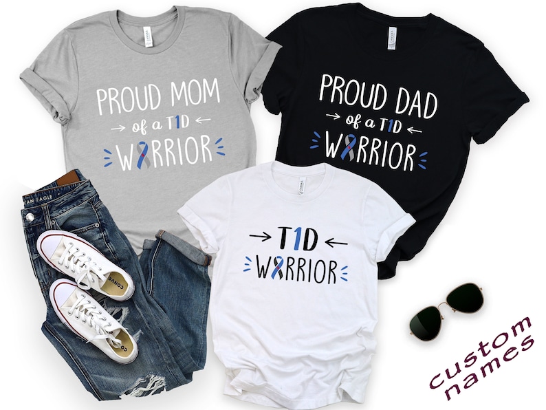 May include: Three t-shirts with the text "Proud Mom of a T1D Warrior", "Proud Dad of a T1D Warrior", and "T1D Warrior" with a blue ribbon graphic. The shirts are gray, black, and white. The text "Custom Names" is visible in the bottom right corner.