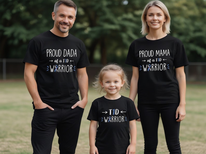 May include: Three black t-shirts with white text and a blue ribbon design. The shirts say "Proud Dada of a TID Warrior", "Proud Mama of a TID Warrior", and "TID Warrior".