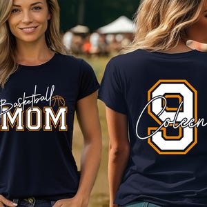 May include: Navy blue t-shirt with the words "Basketball MOM" in white and orange lettering, and a basketball graphic. The back of the shirt displays the number 9 in white with an orange outline and the name "Coleen".