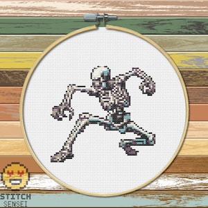 May include: A pixelated cross-stitch pattern of a skeleton in a dancing pose. The skeleton is white with gray and blue accents. The pattern is framed in a wooden hoop.