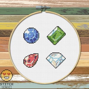 Puede incluir: Patrón de punto de cruz con cuatro gemas de colores: un zafiro azul, una esmeralda verde, un rubí rojo y un diamante blanco.