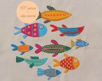 May include: A set of eight colorful felt fish with embroidered details. The fish are various sizes and shapes, with different patterns and colors. The text "PDF pattern + video tutorial" is in a circle at the top of the image.