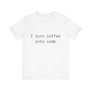 Puede incluir: Camiseta blanca con el texto negro "I turn coffee into code". La camiseta de manga corta tiene un diseño de cuello redondo. El eslogan está impreso en el centro del frente, lo que la convierte en una prenda informal.