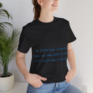 Puede incluir: Camiseta negra con texto azul que dice: "99 little bugs in the code, take one down patch it around, 127 little bugs in the code." La camiseta es de cuello redondo y la lleva una persona.