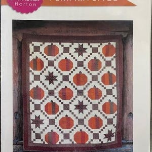 May include: A quilt pattern titled "Pumpkin Spice" by Charisma Horton. The quilt design features orange pumpkins and dark star shapes on a white background, framed by a brown border. The quilt measures 86" x 98".