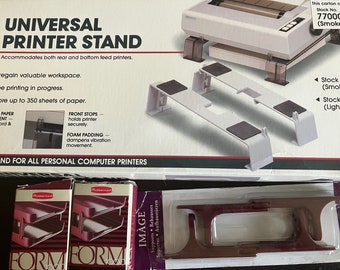 May include: A white printer stand with a black and white printer on top. The stand is made of plastic and has a foam padding to dampen vibration. The stand is designed to hold a printer securely and allow for storage of up to 350 sheets of paper. The box also includes the text "Universal Printer Stand" and "Stand for all personal computer printers".