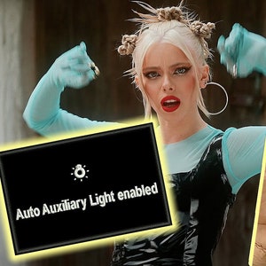 May include: A black screen with white text that reads "Auto Auxiliary Light enabled" and a small icon of a lightbulb. The screen is visible on a camera monitor, which is being held by a person.