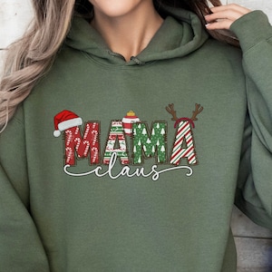 May include: Olive green hoodie with the text "MAMA claus" in a festive design. The word "MAMA" features a Santa hat, Christmas tree, and reindeer antlers. The word "claus" is in a cursive font.