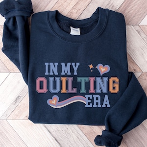 May include: A navy blue sweatshirt with the text "In My Quilting Era" in colorful letters with a rainbow and hearts.