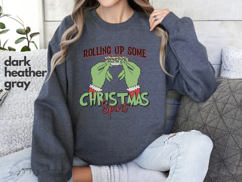 May include: Dark heather gray sweatshirt with a green hand holding a Christmas-themed object and the text "Rolling Up Some Christmas Spirit".