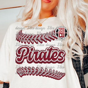 May include: Cream-colored t-shirt featuring the word "Pirates" in maroon script with a white outline. Above and below the word are maroon and white leaf-like designs. The shirt also has the text "design 38co design" in a repeating pattern.