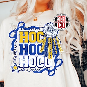May include: White t-shirt with a blue and yellow graphic design. The design includes the text "HOCU HOMECOMING" in a stylized font, a blue ribbon, and a star. A decorative rosette and ribbons are also included.