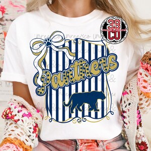 Puede incluir: Camiseta blanca con un dise&ntilde;o azul marino y dorado. El dise&ntilde;o incluye la palabra "Panthers", una silueta de pantera, un lazo con una huella de pata y rayas verticales. Un logotipo es visible en la esquina superior derecha.