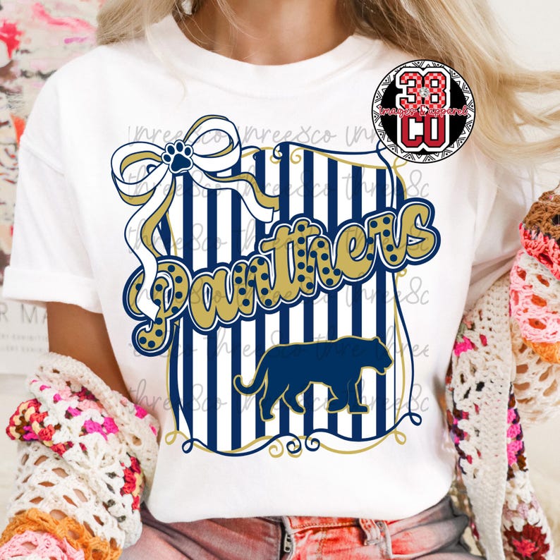 Puede incluir: Camiseta blanca con un dise&ntilde;o azul marino y dorado. El dise&ntilde;o incluye la palabra "Panthers", una silueta de pantera, un lazo con una huella de pata y rayas verticales. Un logotipo es visible en la esquina superior derecha.