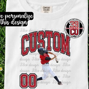 May include: White t-shirt with a baseball theme. The shirt features the word "CUSTOM" in red block letters, a baseball player graphic, and the numbers "00" in red. The text "We personalize this design" is also visible.