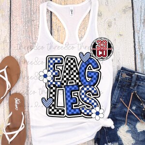 Puede incluir: Camiseta sin mangas blanca con la palabra "EAGLES" en un dise&ntilde;o a cuadros azul y negro. Las letras est&aacute;n delineadas en negro y decoradas con corazones azules y flores blancas. La camiseta sin mangas se combina con pantalones cortos de mezclilla y sandalias.