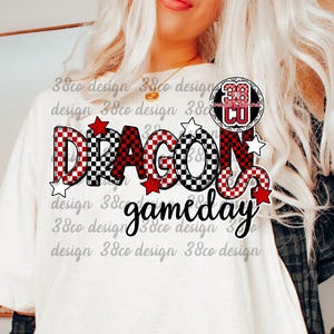May include: White t-shirt with the words "DRAGONS gameday" in a mix of red, black, and white checkered and solid fonts. The design includes red stars and a circular logo with the letters "CU".