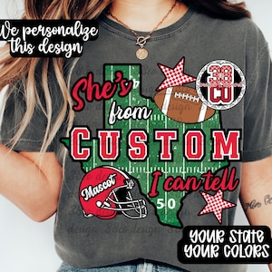 May include: A charcoal gray t-shirt featuring a graphic of the state of Texas with a football field pattern. The design includes a red football helmet, a brown football, red stars, and the text: She's from, CUSTOM, I can tell, 50, Mascot.