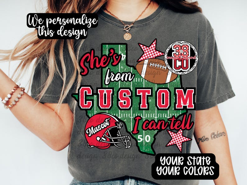 May include: A charcoal gray t-shirt featuring a graphic of the state of Texas with a football field pattern. The design includes a red football helmet, a brown football, red stars, and the text: She's from, CUSTOM, I can tell, 50, Mascot.