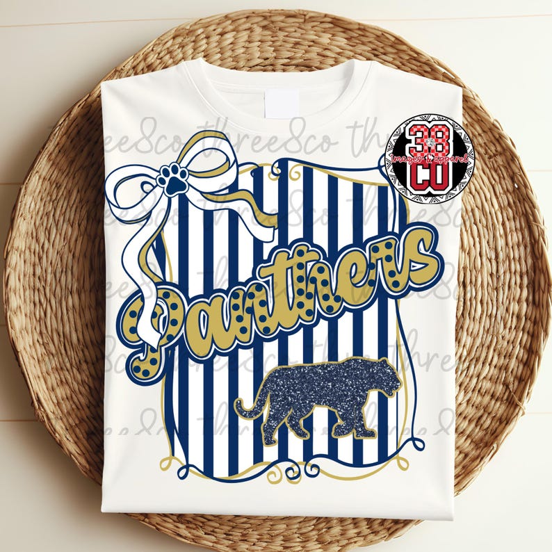 Puede incluir: Camiseta blanca con un dise&ntilde;o con la palabra "Panthers" en dorado, una silueta de pantera azul marino y un lazo con una huella de pata. El dise&ntilde;o incluye rayas azul marino y blancas.