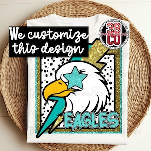 May include: White t-shirt featuring a graphic of an eagle with a teal star and lightning bolt. The word "EAGLES" is in teal, and the text "We customize this design" is in a black box.