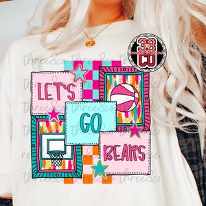 May include: White t-shirt with a colorful basketball-themed graphic. The design includes the words "LET'S GO BEARS" in pink and teal, along with basketball imagery and stars. The shirt has a crew neck.