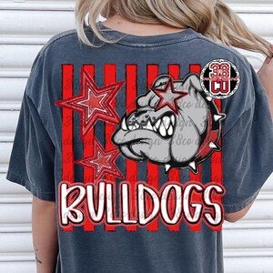 May include: A charcoal gray t-shirt featuring a graphic print of a bulldog head with a spiked collar, two red stars, and vertical red stripes. The word BULLDOGS is printed in large white letters with a red outline at the bottom of the design.