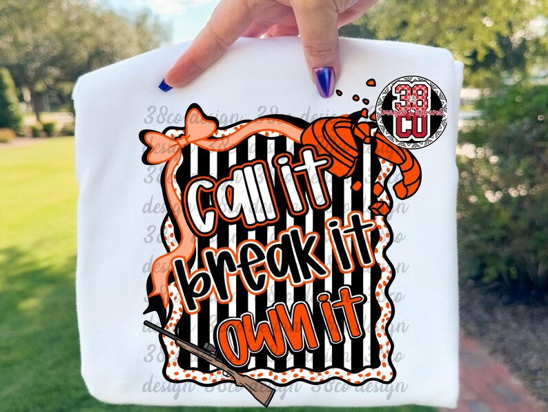 May include: White sweatshirt with a graphic design featuring the words "Call it, Break it, Own it" in a bold, orange and black design. The design includes a shotgun, clay target, and decorative elements.