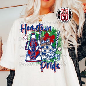 Può includere: T-shirt bianca con un design Hometown Pride. La grafica include un pallone da football, un casco e un megafono da cheerleader, con la parola "Pioneers" e stelle. Il design è in rosso, bianco e blu.