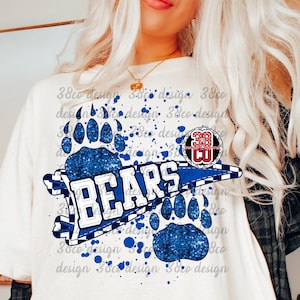 Op de afbeelding: Wit T-shirt met een blauw en wit ontwerp met het woord "BEARS", pootafdrukken en een cirkelvormig embleem. Het ontwerp bevat blauwe verfspatten, waardoor een sportief, collegiaal thema ontstaat.